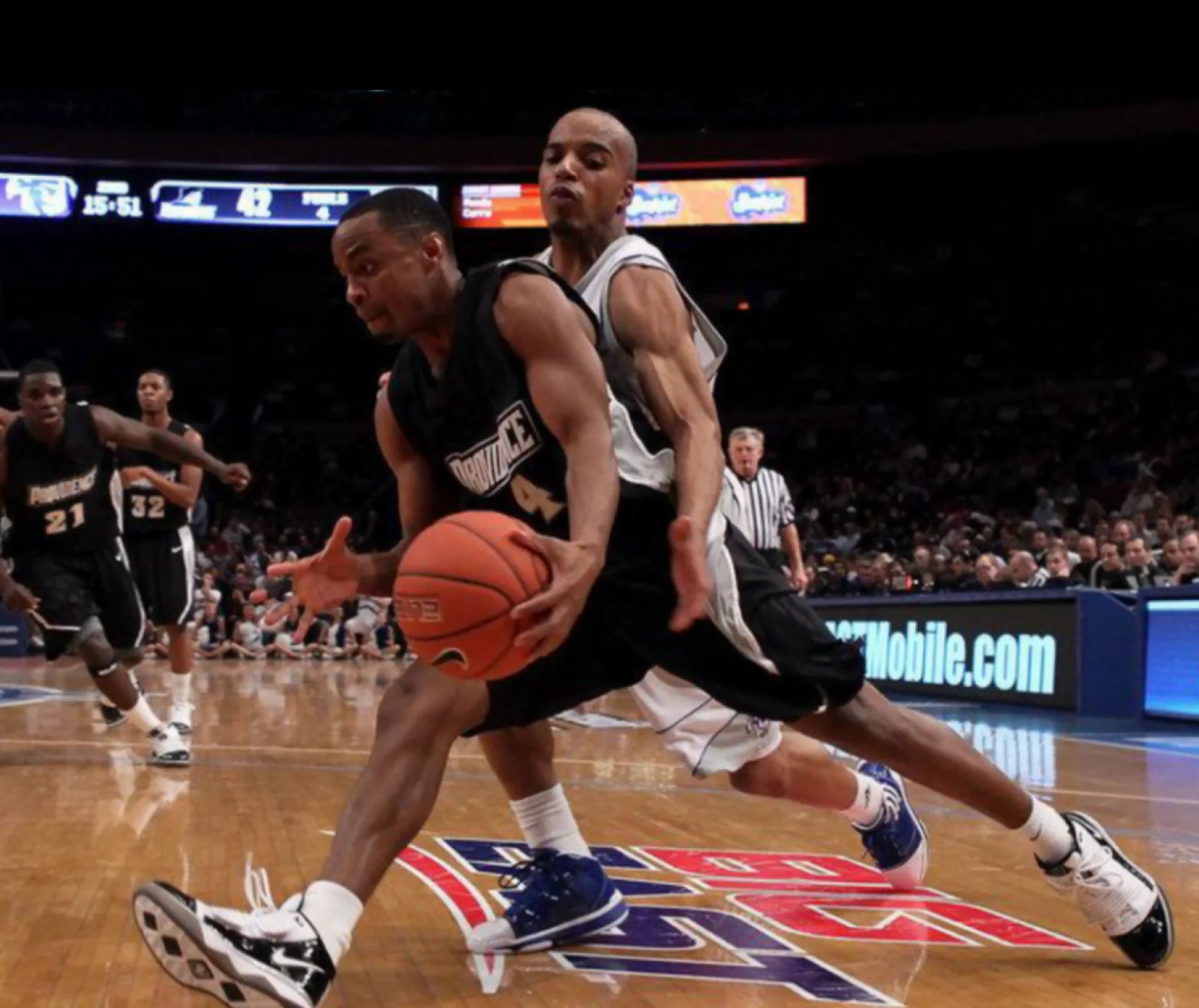 Providence basketball player drives to the basket while protecting the ball from a defender during a college basketball game.